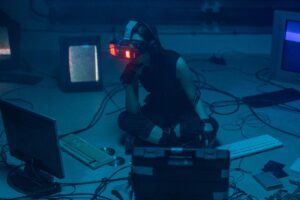 A woman in a dark room wearing a VR headset surrounded by retro technology.